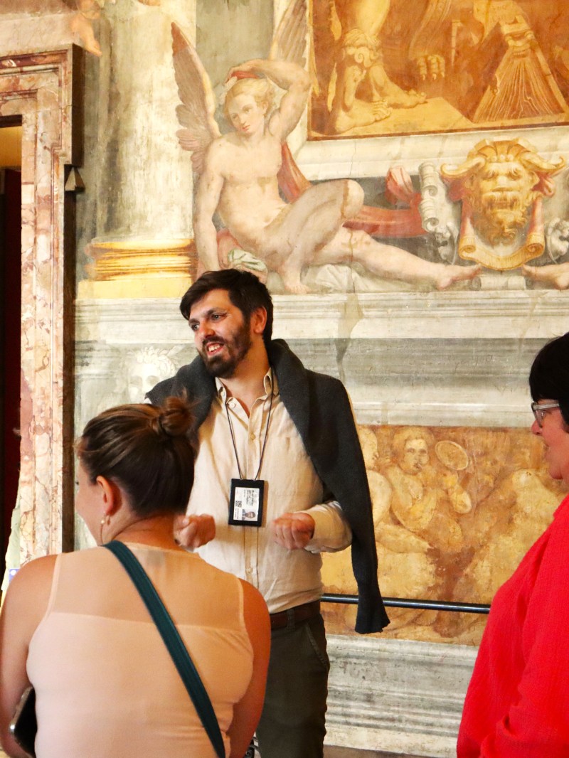 Tour guide explaining fresco to a group in a historic building.