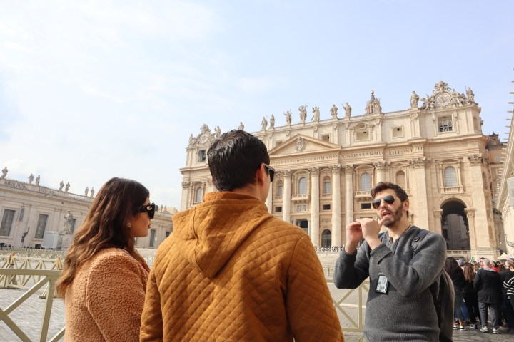 People standing in front of an ornate building with columns and statues on top.