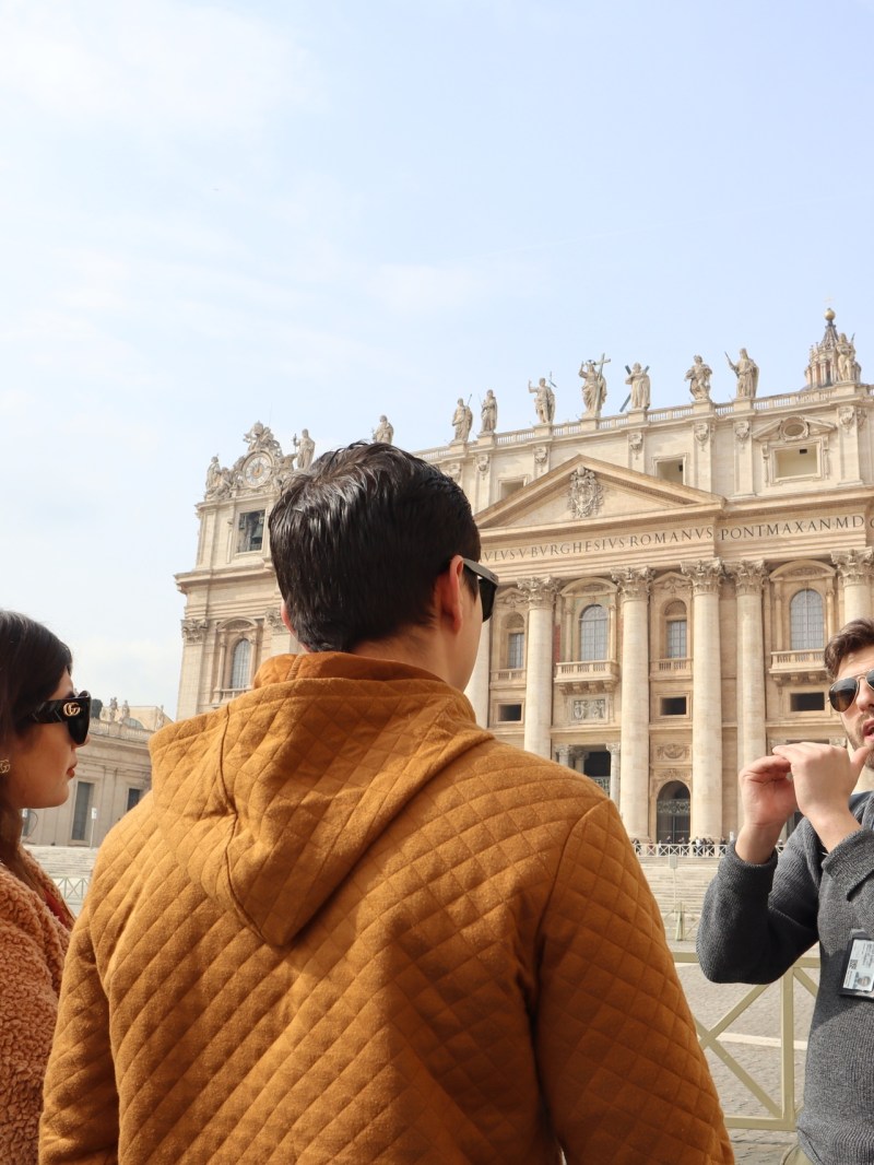 People standing in front of an ornate building with columns and statues on top.