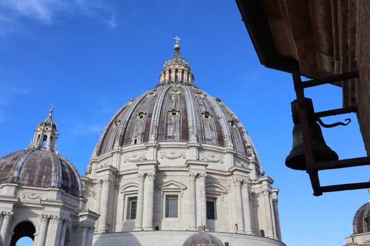 Large domed cathedral with cross, bell visible on right, and blue sky background.