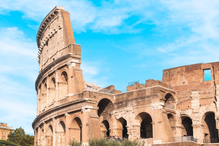 Ancient Roman Colosseum with blue sky and clouds in the background.