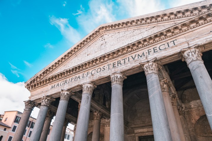 Ancient building facade with columns and Latin inscription against blue sky.