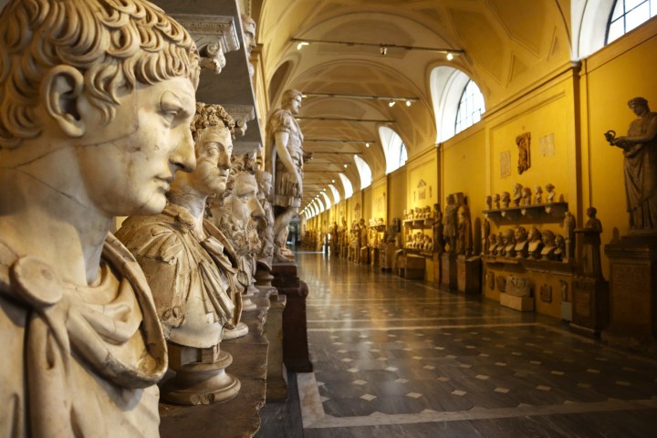 Marble busts line a gallery with arched ceiling and checkerboard floor in a museum.