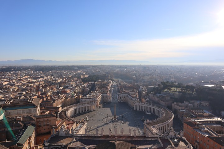 Aerial view of St. Peter's Square and surrounding cityscape under a clear blue sky.